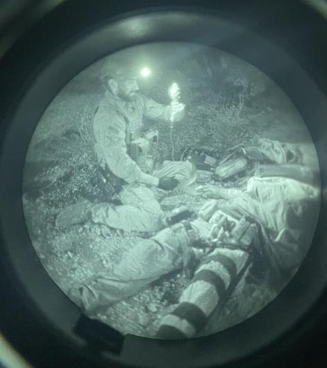 Night-vision view of tactical officers providing medical care during a nighttime training exercise.