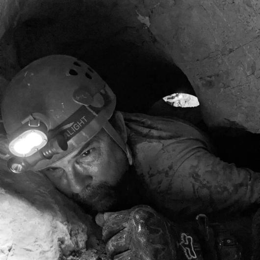 A man in a hard hat crawls through a cave space. 