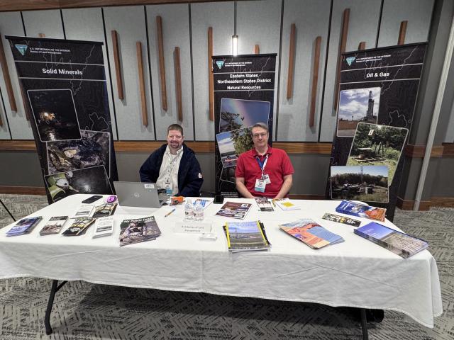 Two men seated behind a table with brochures at a U.S. Department of the Interior Bureau of Land Management informational booth.