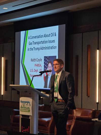 Speaker standing next to a podium during a presentation on oil and gas transportation issues in the Trump administration.
