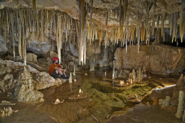 A man sits beneath cave formations in a cave. 