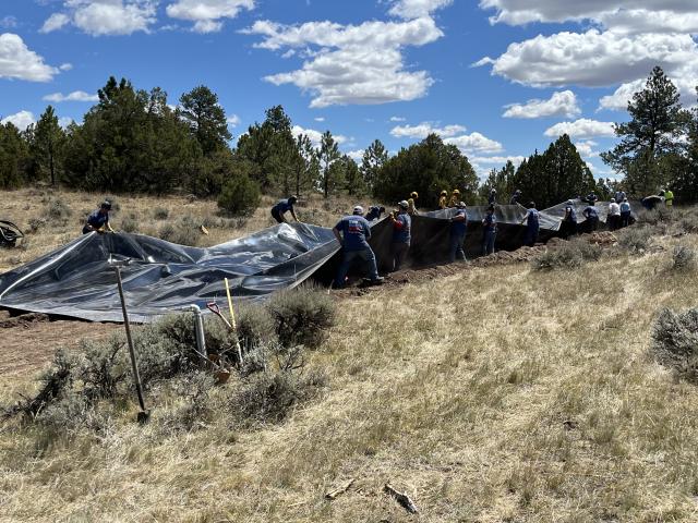a group of people holding a long length of black plastic in a grassy field