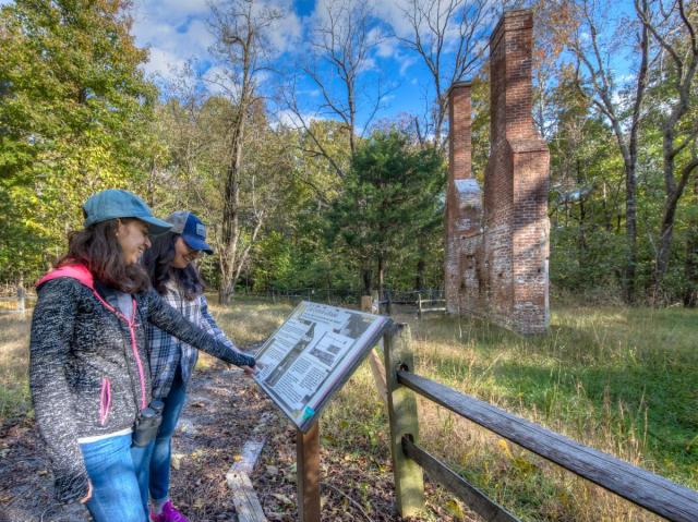 Visitors read an interpretive sign at the remains of a historic brick ruins of the colonial-era Chiles homesite.