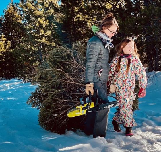 Mother and daughter dragging Christmas tree on snow