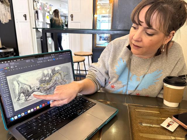 photo of a woman pointing to an illustrated dinosaur scene on a laptop computer screen