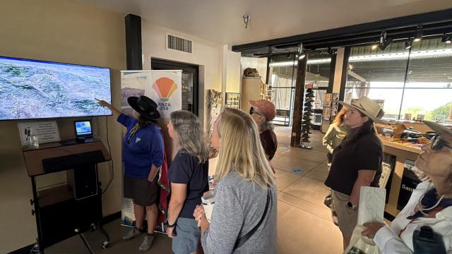 People in a visitors center look at a map displayed on a TV.