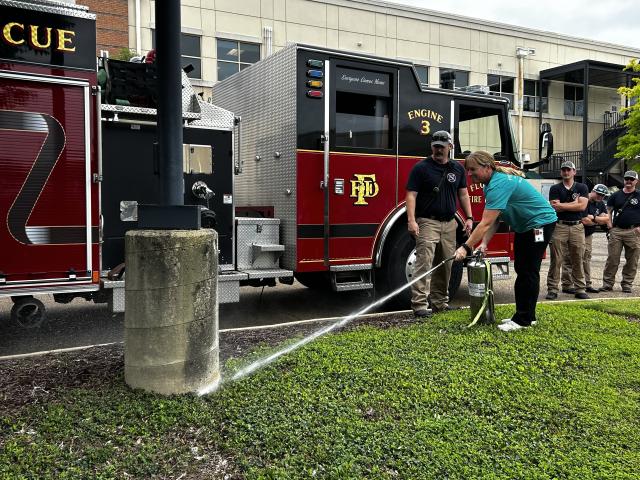 A local firefighter guides Wild Horse and Burro Compliance Specialist, Megan Velasquez, through using a fire extinguisher during a hands‑on safety demonstration.