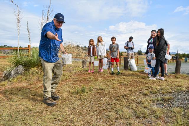 BLM staff show how to plant seeds to a group of kids holding buckets at a National Public Lands Day event in New Mexico in 2024.