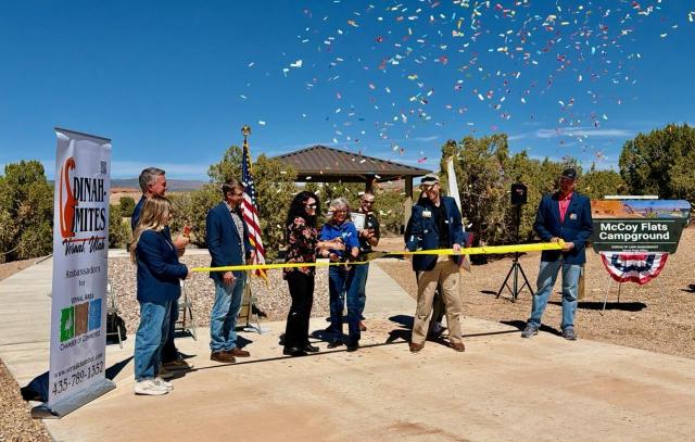 Nine people standing behind a ribbon as it is being cut in the campground. 