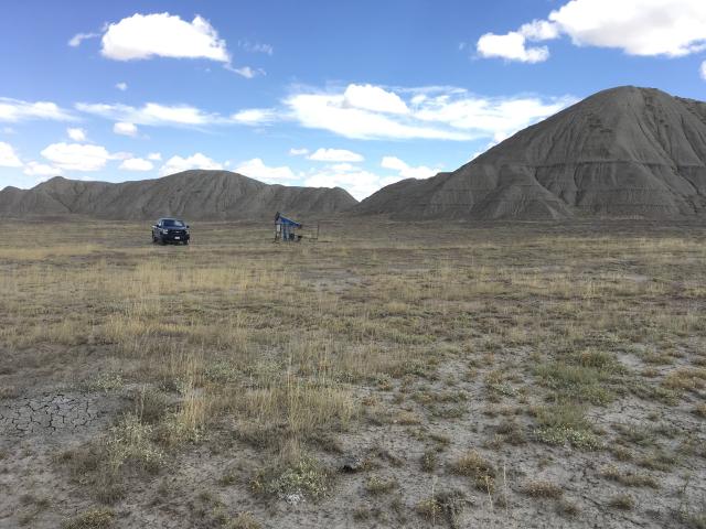 a truck sits next to an oil pumpjack in a field with mountain in the background