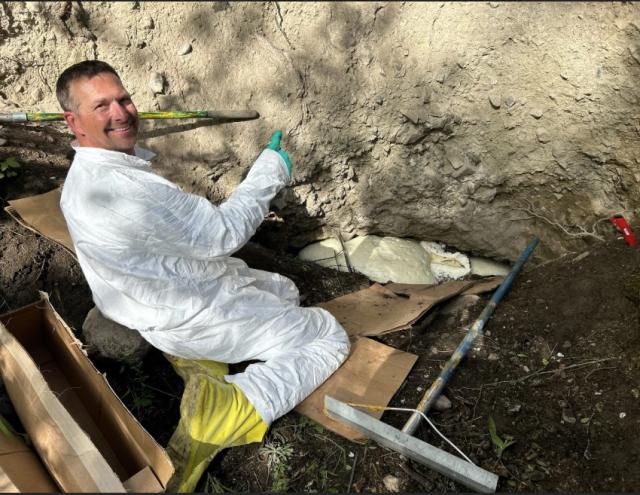 Person in a white protective suit working at the base of an eroded soil bank with foam material filling a void.