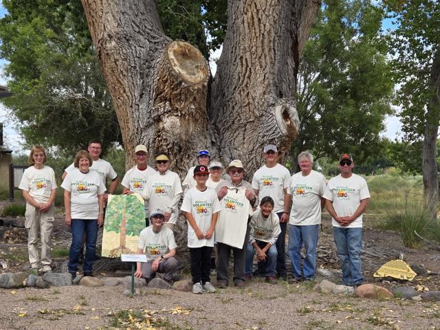 a group of people in National Public Lands Day Volunteer t-shirts stand under a large cottonwood tree