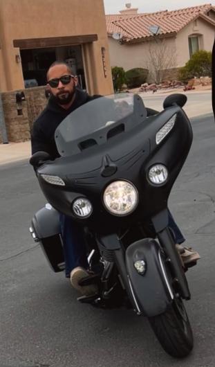 A young man with sunglasses on a black motorcycle.