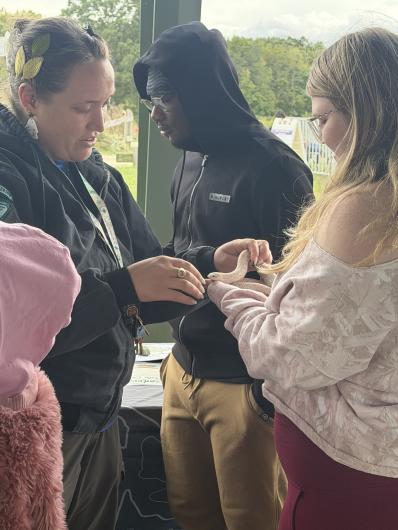 Participants gather around a Bureau of Land Management educator as a child gently touches a light-colored snake during an outdoor environmental education activity.