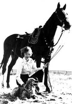 Wild horse annie kneeling next to a horse and a dog. 