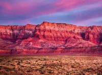 Clouds are pink and blue above red-orange cliffs.