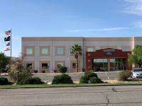 An office building with windows, an asphalt parking lot, and a flag pole flying flags.