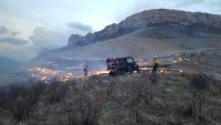 Two firefighters monitor a prescribed burn on a ridge. An ATV stands between them.