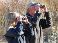 two people hold binoculars to their eyes