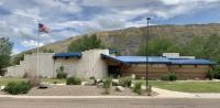 Photo. A view of the entrance to the Missouri Breaks Interpretive Center. The building structure was designed to represent the Missouri River’s famous White Cliffs area and layers of different-colored sediment found in other portions of the cliffs along the river. The blue roof represents the sky. 