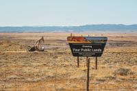 A sign that says "Entering Your Public Lands" In the foreground with an oil derrick in the background on BLM lands