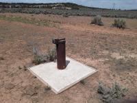 groundwater monitoring well, a pipe sticks out of a small cement pad in desert scrubland