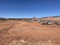 A flat red dirt area extends to the horizon with scattered trucks and campers