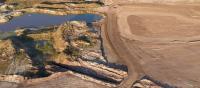 Aerial view of a barren landscape featuring small ponds, dirt mounds, and a cleared area, showing signs of excavation and mining activity.