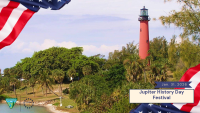 Tall red lighthouse surrounded by green trees under a clear sky with American flags framing the scene for Jupiter History Day Festival.