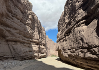 slot canyon with gravel trail and rock walls and a blue sky peaking through.