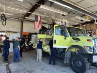 Fire fighters look in cabinets and attach a hose to the top of a wildland firefighting engine in a firehouse engine bay
