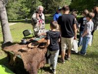 A student stands at an outdoor table that is covered in animal pelts and archeological artifacts
