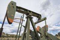 An oil pump jack that's painted green with orange trim is seen with a cloudy sky in the background.
