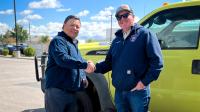 Erik Valdez shakes hands with a smiling Snowville firefighter wearing a navy hoodie and sunglasses in front of a lime-green Ford F-550 wildland engine.