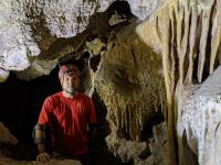 A man sits in a cave next to cave formations. 