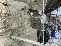 A person standing on scaffolding sprays paint onto a rock face.