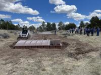 a group of people stand near a brown structure in the ground with machinery and dirt around it
