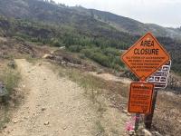Photo of trail with closure sign and charred timber in background
