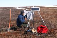 BLM staff setting up data collection equipment on an area in the NPR-A covered in tundra with patches of snow still on the ground.