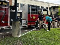 A local firefighter guides Wild Horse and Burro Compliance Specialist, Megan Velasquez, through using a fire extinguisher during a hands‑on safety demonstration.