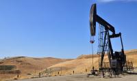 An oil derrick in dry, grass hills