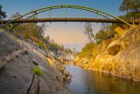 A large green bridge over a granite gorge at sunset