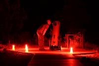 Man gazes through a large telescope, surrounded by red lights.