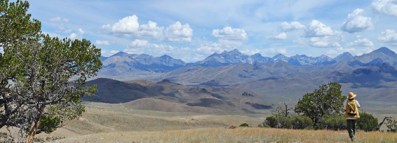 A vast landscape with rolling hills and distant mountain ranges under a partly cloudy sky.