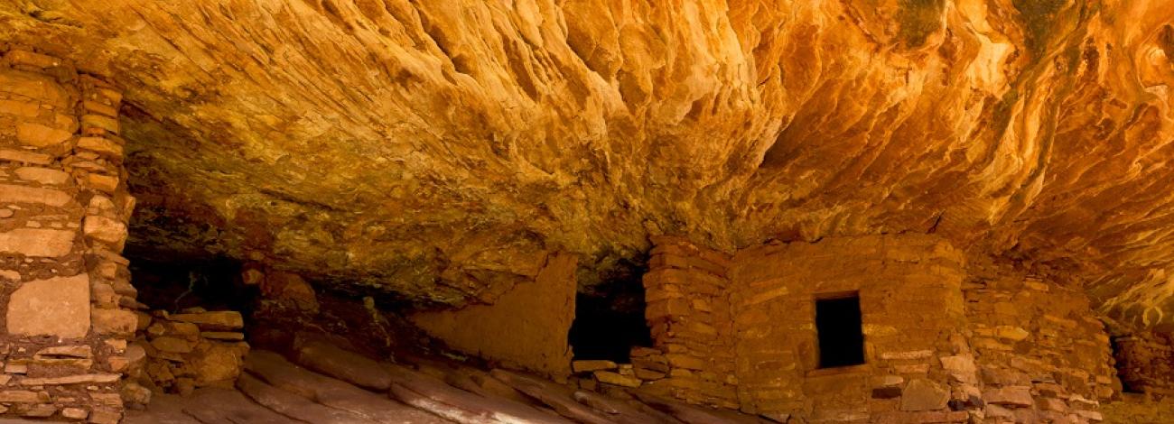 Ancient cliff dwellings built into a rocky overhang with stone walls and small rectangular windows.