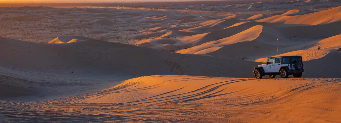 A jeep  overlooks a  sea of dunes at sunset