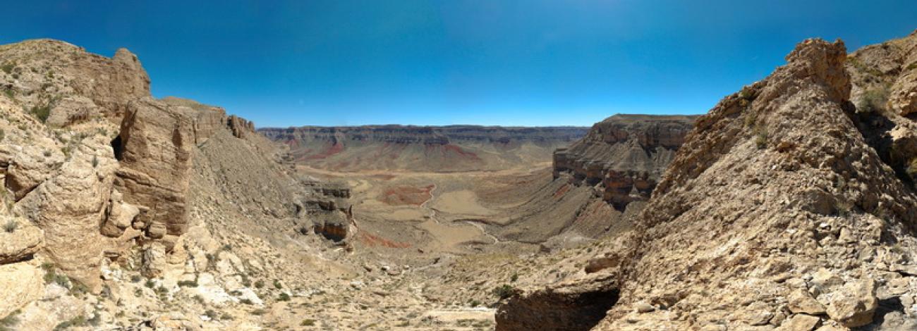 A birds eye view of a remote, tranquil desert with towering canyon walls and a dry streambed meandering through the valley below.
