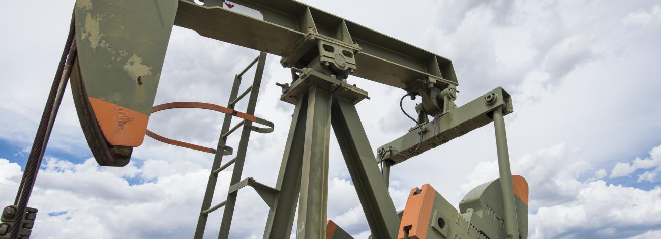 An oil pump jack that's painted green with orange trim is seen with a cloudy sky in the background.
