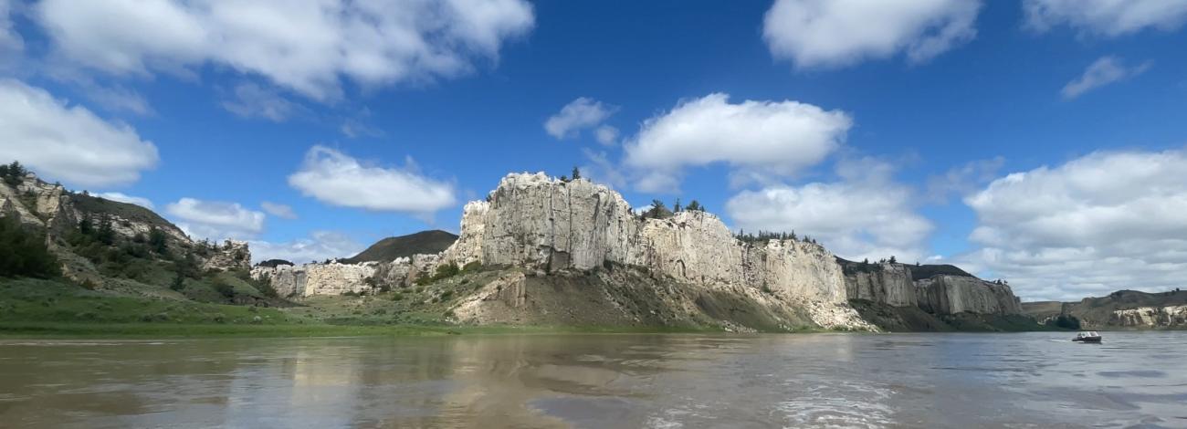 Dramatic white cliffs of the Upper Missouri River Breaks National Monument rising above the waters of the Missouri River under a bright blue sky.