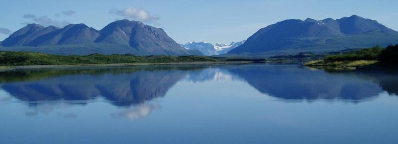 A scenic view of a large lake with mountains and blue sky in the background.